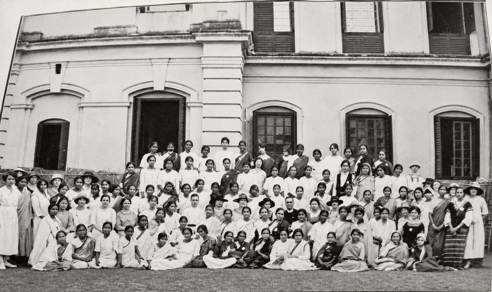 Group photograph of YWCA members, rows of women seated and standing in front of a large colonial-era building