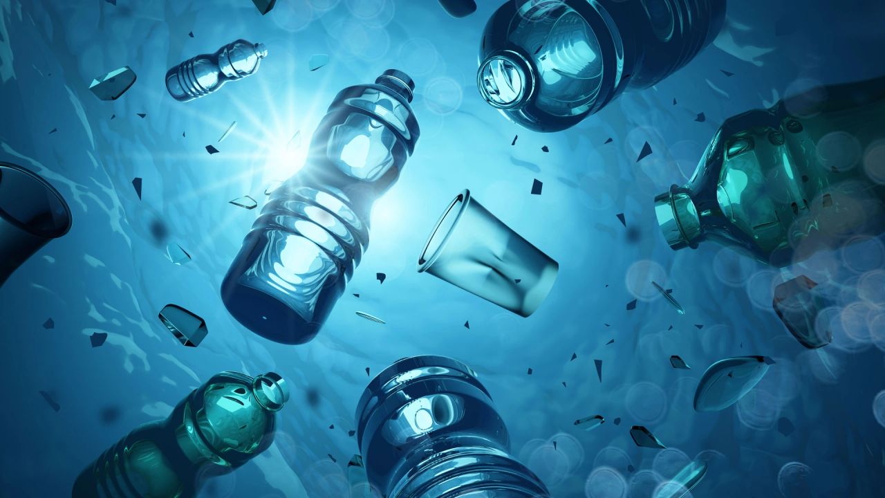 Plastic bottles, a plastic cup and broken plastic fragments drifting through blue water, with sunlight bursting through from above.