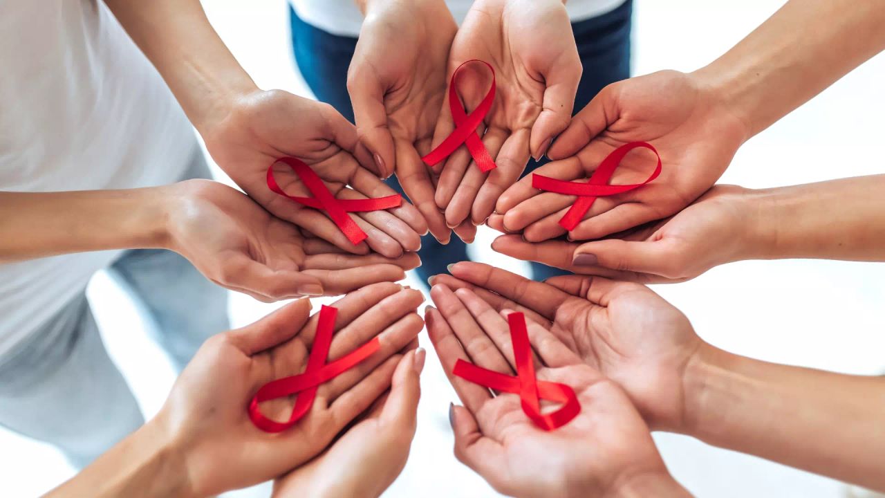 Open hands in a circle, each holding a red AIDS awareness ribbon.